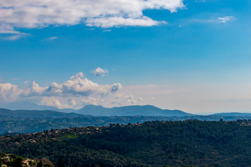 A wide / high angle panoramic view of the low Alps mountains hills covered with forests and remote buildings with hazy multilayered mountain ranges in background (French Côte d'Azur/Provence/Riviera)