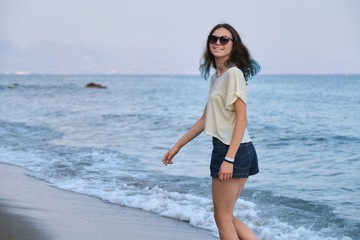 Trendy girl with blue hair in sunglasses walking along sea beach