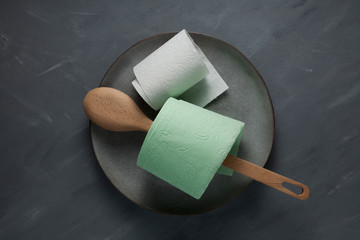 Wooden spoon and rolls of toilet paper on a gray plate. Concept on the topic of hunger, deficiency, madness and panic. Closeup. Copy space
