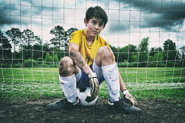 Male child soccer player sitting in the muddy goal