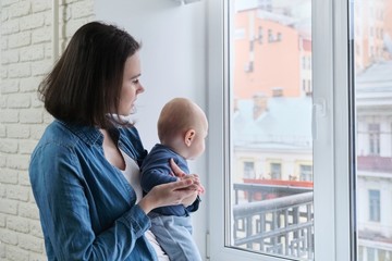 Mother holding baby in arms standing at home near window