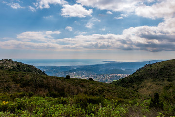 Fototapeta na wymiar A panoramic view of several towns and their buildings densely covering the coastline behind the low Alps mountains hills with the Mediterranean Sea on the horizon (Provence / Riviera / Côte d'Azur)