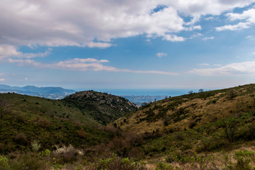 A panoramic view of the low Alps mountains hills with the Mediterranean Sea and several towns' buildings densely covering the coastline on the horizon (Provence / Riviera / Côte d'Azur)