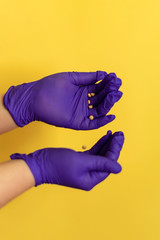 Woman's hands in purple gloves. Pill tablets into her hands. Nurse Protection Against Virus. Pandemic. Coronavirus. Covid-19. yellow background