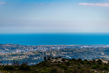 A panoramic view of urban buildings and populated areas densely covering the coastline behind the low Alps mountains hills with the Mediterranean Sea on the horizon (Provence / Riviera / Côte d'Azur)