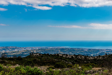 A panoramic view of urban buildings and populated areas densely covering the coastline behind the low Alps mountains hills with the Mediterranean Sea on the horizon (Provence / Riviera / Côte d'Azur)