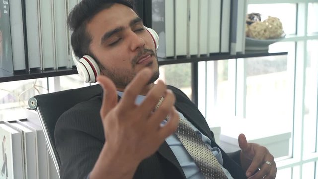 A young businessman singing and listening to music in the office. 