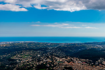 A wide / high angle panoramic view of buildings of several towns (including Vence) covering the low Alps mountains hills and the Mediterranean Sea coastline (French Côte d'Azur/ Provence/ Riviera)