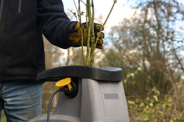 Man is chopping pruning waste with an electric garden shredder, clearing up old branches, copy space