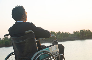 Young disabled man with river background.He is sitting on wheelchair and looking into...