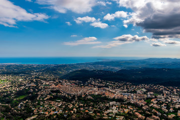 Fototapeta premium A wide / high angle panoramic view of Vence buildings and other towns covering the low Alps mountains hills with the Mediterranean Sea coastline on the horizon (French Côte d'Azur/ Provence/ Riviera)