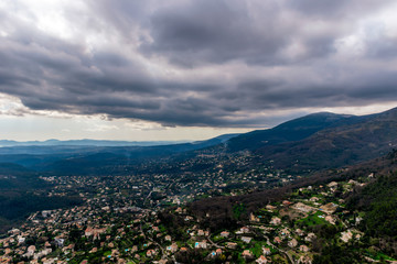 A wide / high angle panoramic view of houses and other buildings of several towns covering the low Alps mountains hills with the mountain ranges in the haze (French Côte d'Azur/ Provence/ Riviera)