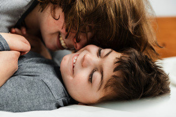 niño caucasico con pluridiscapacidad en pijama y su madre jugando, riendo, haciendo mimos,...