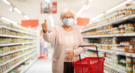 Elderly woman shopping in a supermarket with a protective face mask showing thumbs up