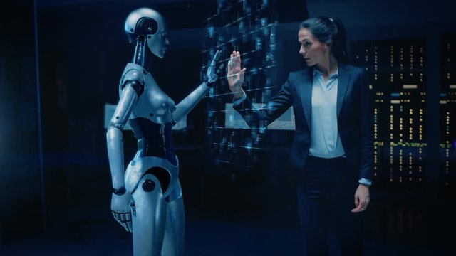 Beautiful, Confident Female Engineer Touching Hands with Humanoid Robot Activating Collaboration, Teamwork Protocol. Computer Artificial Intelligence Concept: People and Robots Working Together