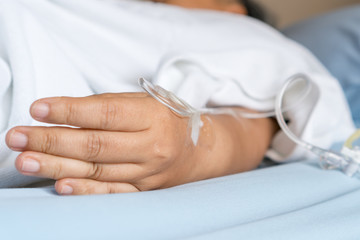 Patients saline, Iv drip, young woman hand with medical drip intravenous needle, give salt water on hospital bed. intravenous therapy (IV) is a therapy that delivers fluids directly into vein.