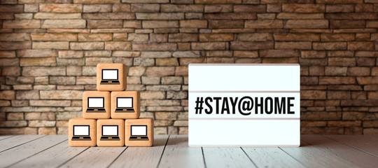 lightbox with message #STAY@HOME and cubes with computer symbols in front of brick wall on wooden floor