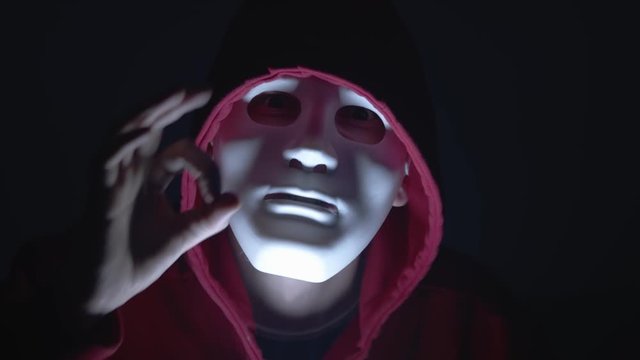 Anonymous hacker with mask and hoodie. Hand gesture showing you are being spied