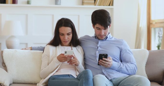 Young couple technology addicts obsessed with mobile phones sitting on sofa. Millennial man and woman overuse smartphones social media ignore each other. Internet addiction problem. Phubbing concept