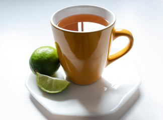 A yellow mug with Colombian traditional hot drink knowed as AGUA DE PANELA with lemon and white background. This hot drink is useful to a illness and its used to a meal too.