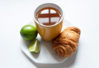 A top view of a yellow cup with Colombian traditional hot drink knowed as AGUA DE PANELA with lemon, one bread and white background. This hot drink is useful to a illness and its used to a meal too.