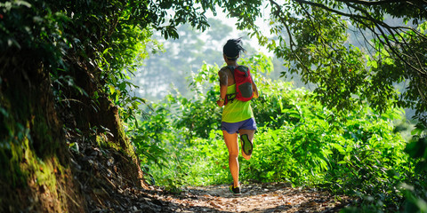 Naklejka na ściany i meble Young woman trail runner running in sunrise tropical forest