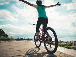 Hands free cycling woman riding Mountain Bike on sunrise seaside