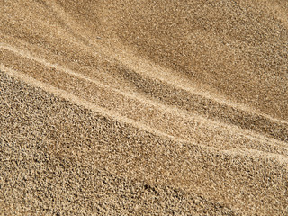 Background from a large number of brown-yellow barley grains, with waves, side view.