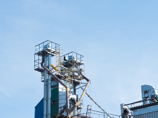 The upper metal part of the complex for processing grain with a large number of pipes against a blue sky.