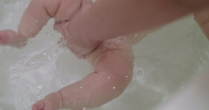 View of newborn legs swimming in water during bathing