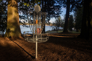 Disc golf basket on pretty park course near a lake under blue sky