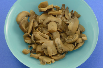 Close up on freshly rinsed canned mushrooms in blue bowl on darker blue background