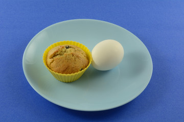 Quick on the run breakfast of blueberry muffin in silicone muffin cup and hard boiled egg on blue plate