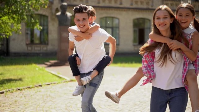 Happy smiling family walking through city garden or park at sunny day by ancient building, piggy back ride. Young happy family enjoy their free vacation time together with kids. Family love concept.