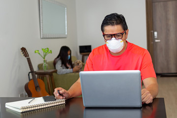 A man with a mask works on his computer at home