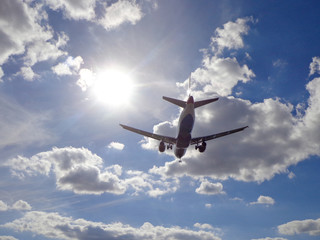 Commercial Aircraft Flying Overhead with Sun and Clouds in Distance