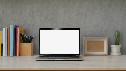 Close up view of modern workspace with blank screen laptop, decorations, books and stationery