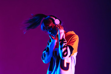 Stylish fashion teenager model wearing hoodie and headphones listening dj music dancing in purple...