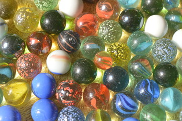 The glass balls are of many colors that are placed on a yellow cloth.