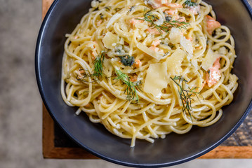 A serving of Salmon Spaghetti in a plain blue round bowl on a wooden table