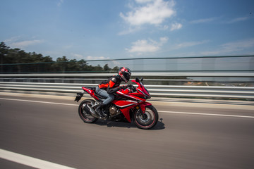 Fototapeta na wymiar Biker in helmet and gear biking a motorcycle on the bridge under the blue sky
