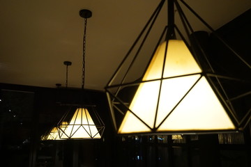 Closed up yellow modern design lamps with Edison burb in cafe at night. Hanging bulb lamps. Chandelier with yellow LED lighting elements covered with metal wire frame lampshades