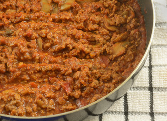 Hot sloppy Joe hamburger mix with canned mushrooms in pan with dish towel