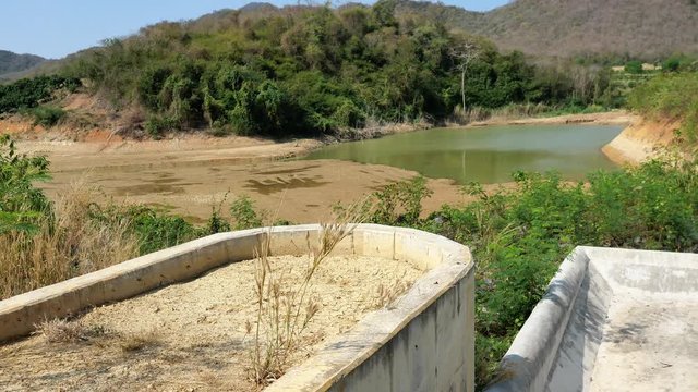 Dry spillway with small amount of water in the dam with mountain and blue sky and white cloud in background , Drought in Thailand	