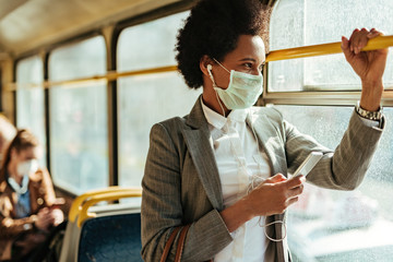 African American businesswoman with face mask texting on the phone while traveling by bus.
