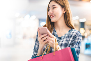 Smiling young Asian woman with shopping colour bags over mall background. using a smart phone shopping online  and smiling while standing mall building. lifestyle concept