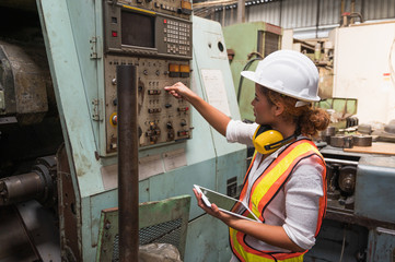 Female industrial worker working and checking machine in a large industrial factory with many equipment.