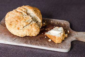 rustic homemade herbs and sesame bread just out of the oven on cutting board with knife and slice cut out