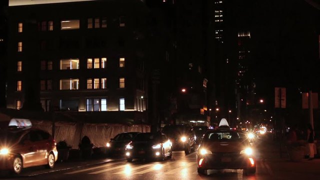 New York City Night Traffic With Car Lights On. Yellow Taxi Cabs And Other Cars Driving Off Screen Close To Camera. 