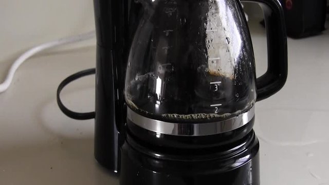 Coffee Brewing And Filling Up The Small Coffee Pot.  There Is Small Amount Of Black Coffee In The Pot.  Coffee Pot Is On The Kitchen Counter In The Morning Hours.  Close-up Zoom.